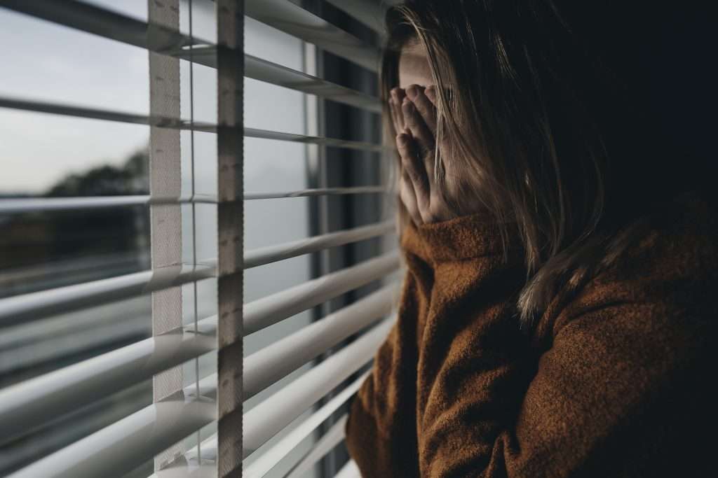 Trauma responses - worried women covering face standing by window