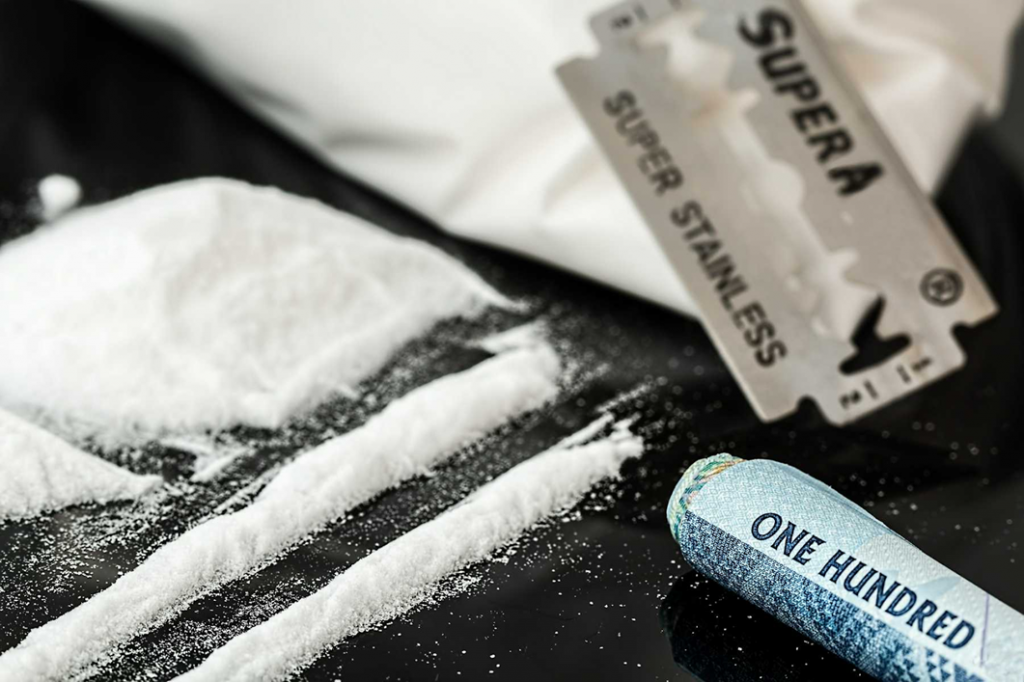 Lines of cocaine with stainless steel razor blade and rolled up hundred dollar bill. Shows what cocaine looks like.