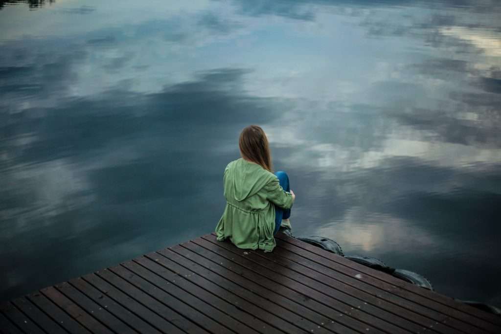 Woman sitting on the edge of a dock on a lake. Depicts: Most Common Concurrent Disorders With Addiction