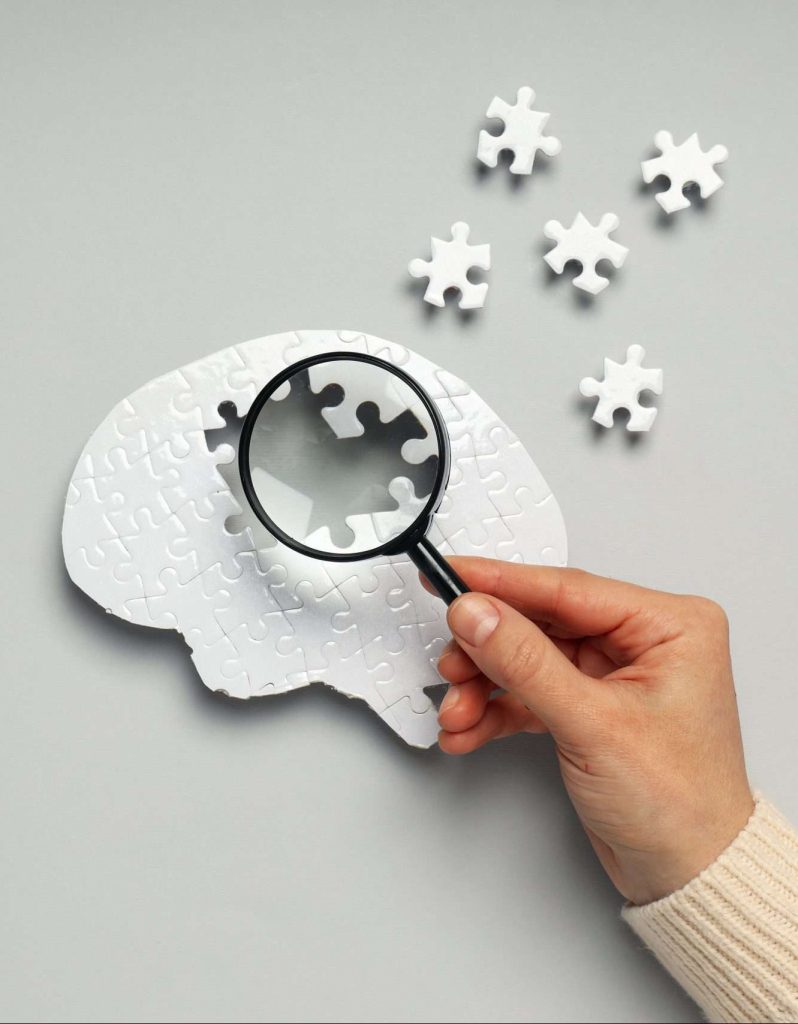 A puzzle designed in the shape of a brain with pieces removed and someone holding a magnifying glass over it, ADHD, ADHD Treatment Toronto, What is ADHD, Signs and Symptoms of ADHD, ADHD Counselling, ADHD Clinic, ADHD Treatment Ontario