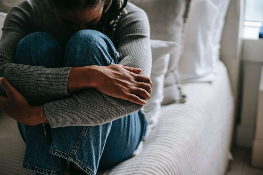 Woman embracing knees on bed, represents hangxiety