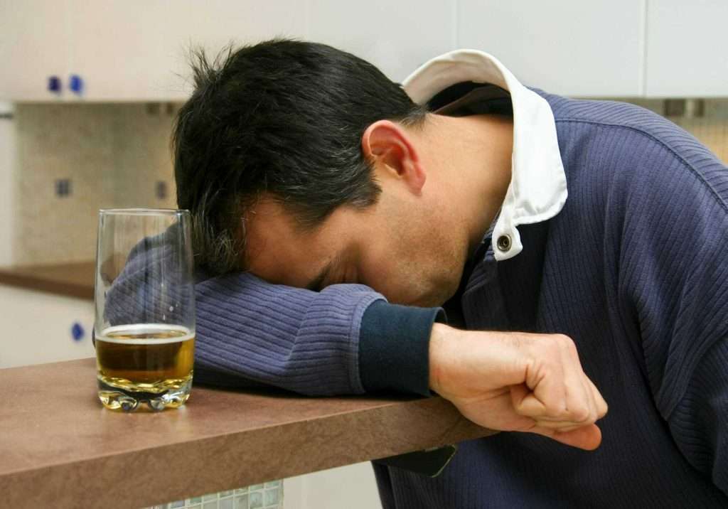 Person hungover laying their head on a table with a half-empty glass of alcohol. How to get alcohol out of your system, How to flush alcohol out of your system, Does alcohol cause inflammation, How to stop diarrhea after drinking alcohol, Does alcohol dehydrate you