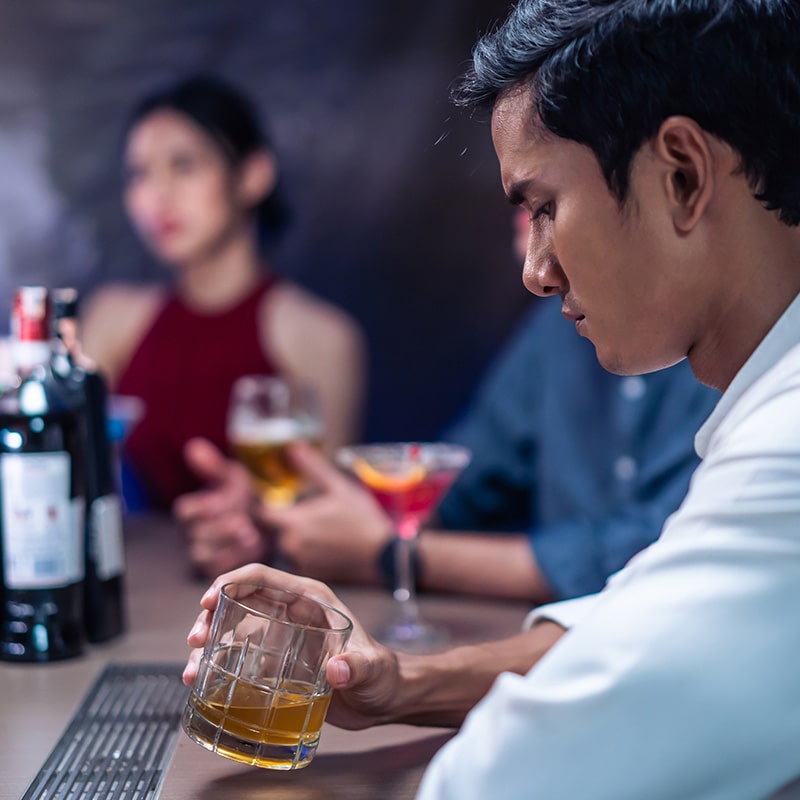 Man at a bar drinking and looking down as he struggles with Alcohol Addiction and considers alcohol rehabilitation